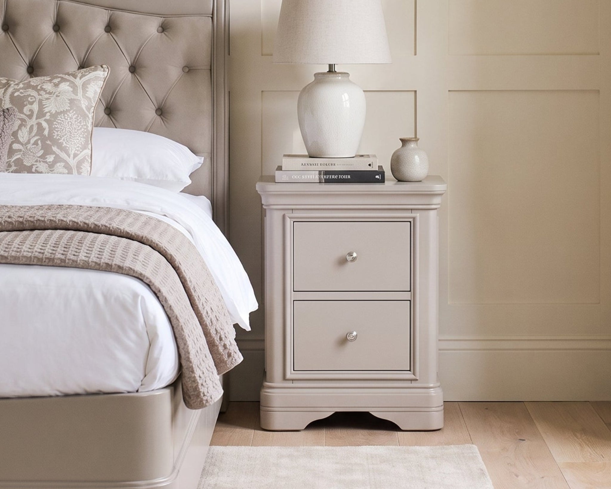 Neatly made bed with a nightstand featuring a lamp and decor items in a bedroom setting.