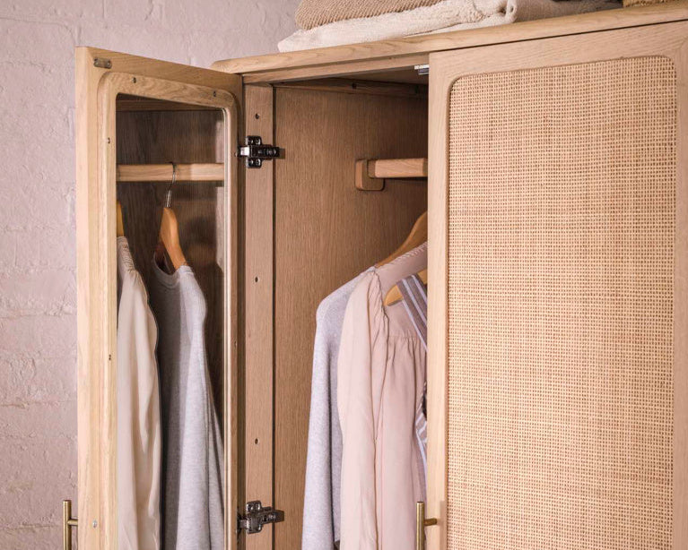 Open wardrobe with clothes hanging inside against a neutral wall.