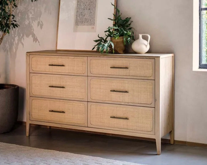 Beige rattan dresser with six drawers in a room with plants and a window.