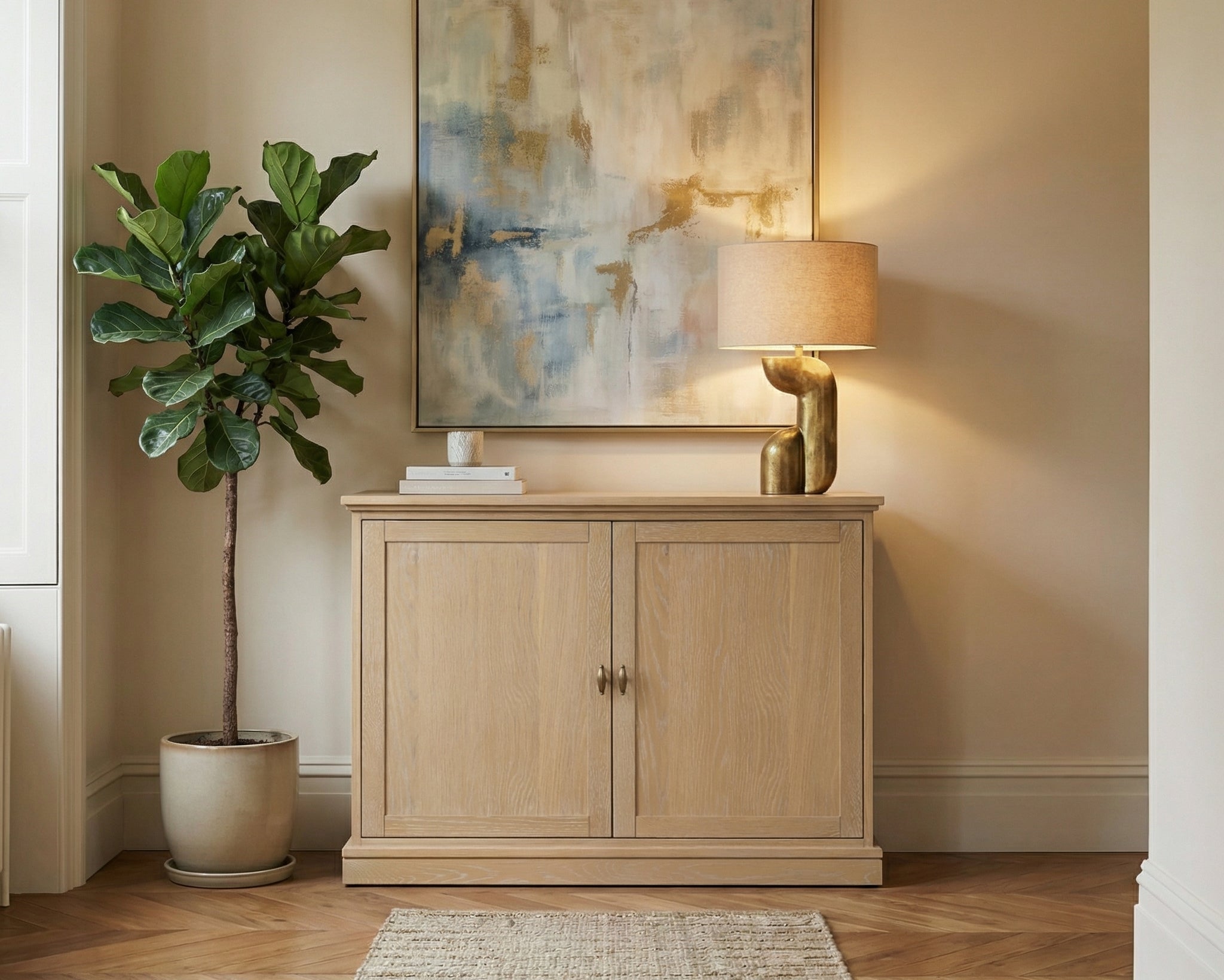 Light wood cabinet with a lamp and abstract painting in a room with a plant and rug.