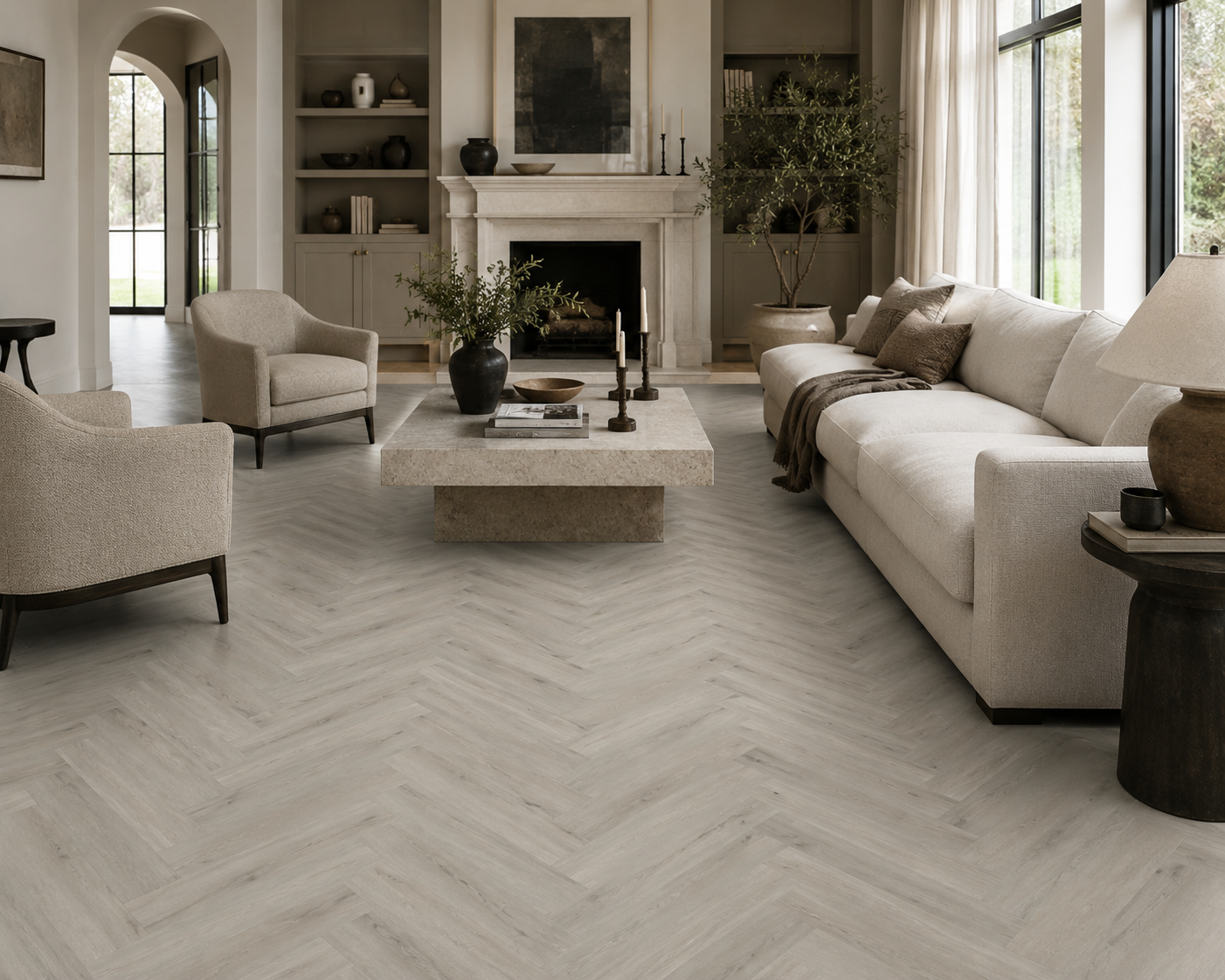 A bright, modern living room with light gray herringbone wood flooring, featuring a cream sofa, matching armchairs, a stone coffee table, and a fireplace in the background.