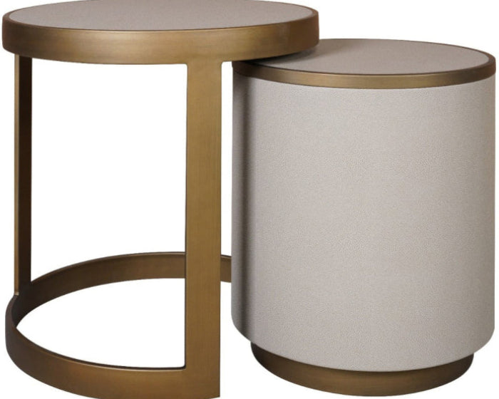 A modern nesting side table set featuring a round brass-finished metal table with an open frame and a matching cylindrical ottoman-style side table with a light beige upholstered cylinder and brass base.
