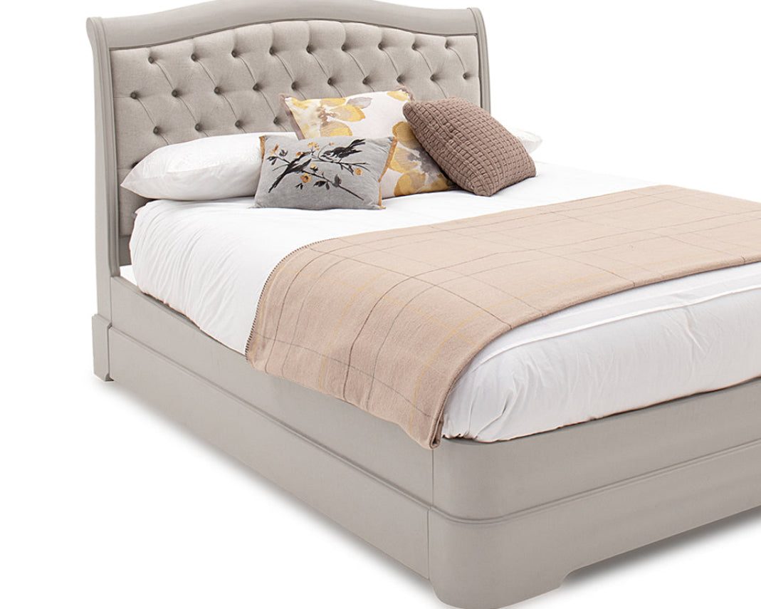 Beige upholstered bed with white bedding and decorative pillows on a white background