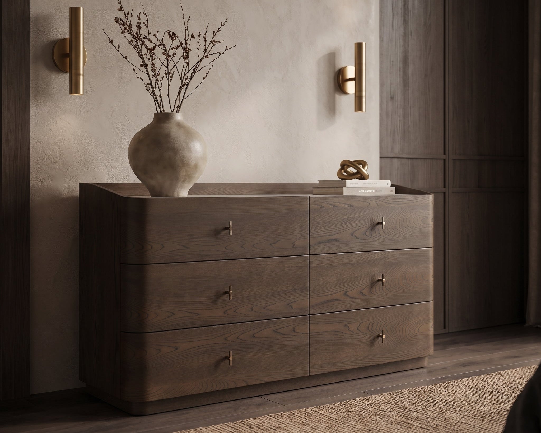 A dark brown wooden dresser with six drawers and small brass handles, styled in a bedroom setting with a ceramic vase, dried branches, and books on top.