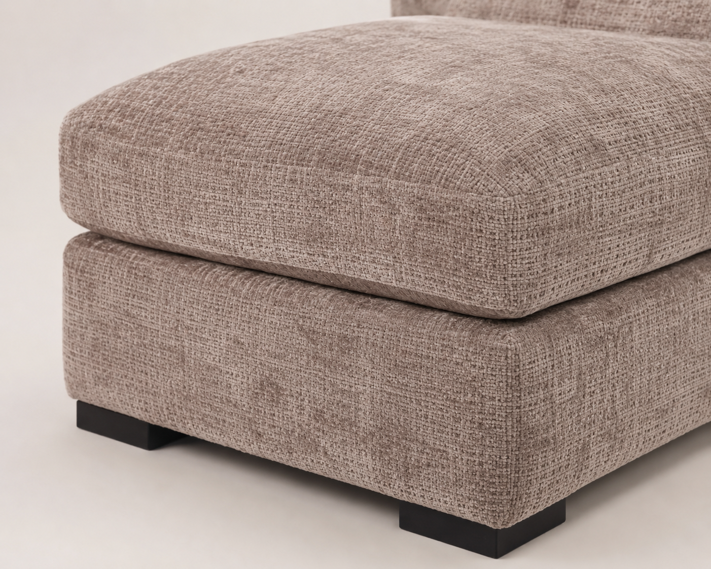 A close-up of a modern upholstered ottoman or seat module with a textured taupe fabric and dark block feet, shown on a light neutral studio background.