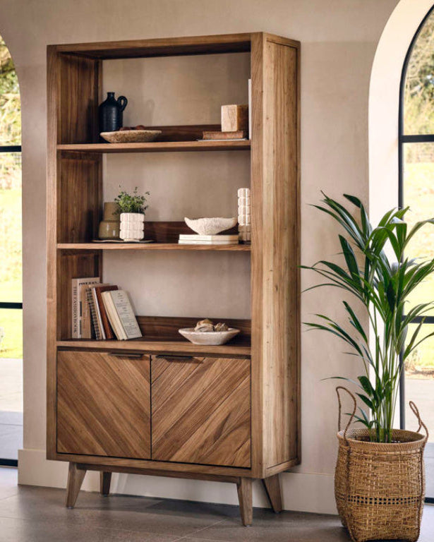 Wooden bookshelf with decorative items in a room with large windows.