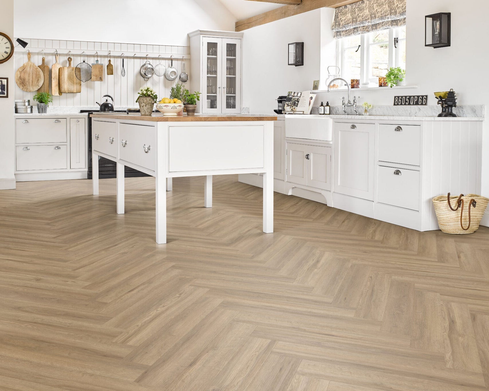 Light oak herringbone parquet flooring installed in a bright, modern white kitchen with a central island and wooden countertops.