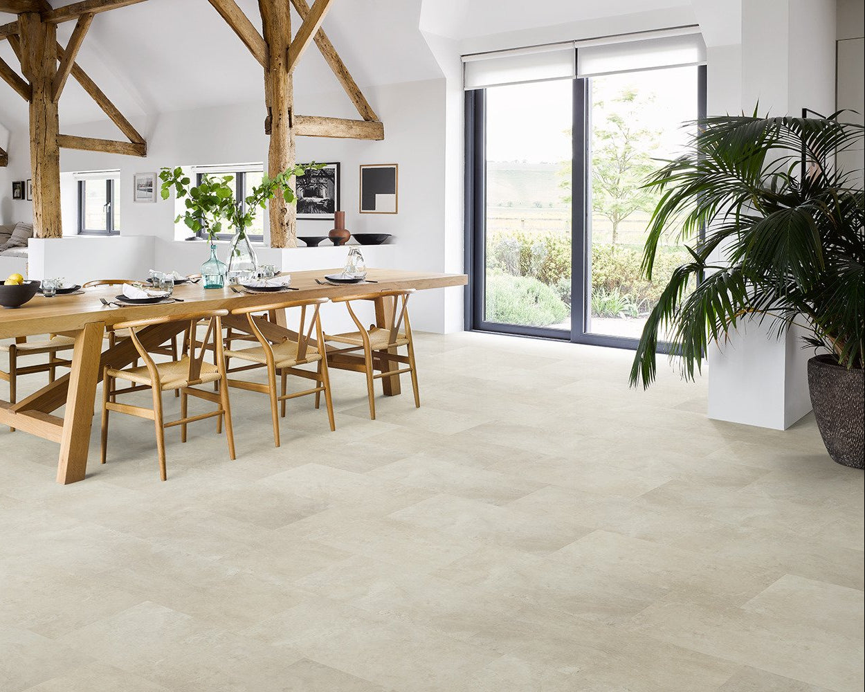 Light beige stone-look floor tiles in a bright, modern dining room with a wooden dining table and chairs, large windows, and a potted plant.